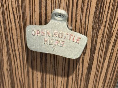 Vintage cast iron bottle opener mounted on weathered wood wall with embossed text OPEN BOTTLE HERE and arrow pointing down, rustic pub decoration