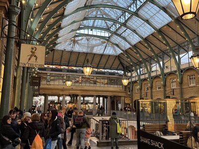 Two-story Covent Garden Market interior with Victorian green iron framework, glass roof, Shake Shack on ground floor, upper balcony with shops