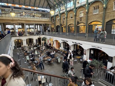 View from upper level of Covent Garden Market looking down at restaurant terraces, wooden tables and chairs, Wine Place and Tapas Stories signage