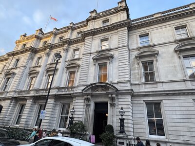 Neoclassical government building with cream stone facade, multiple window bays across several floors, Union Jack flag on rooftop, ornate balustrade, tourists and cars at street level