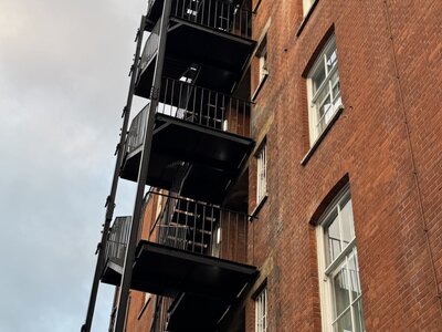 Low angle view looking up at red brick building with dramatic black zigzag fire escape staircase on exterior wall, emphasizing vertical lines