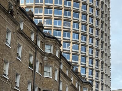 Modern curved glass tower building with horizontal bands rising above historic brick Victorian buildings, striking architectural contrast between contemporary and traditional styles