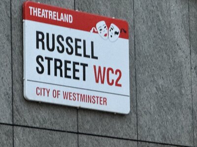 Street sign reading RUSSELL STREET WC2 with red Theatreland banner, white comedy and tragedy mask emblems, City of Westminster designation