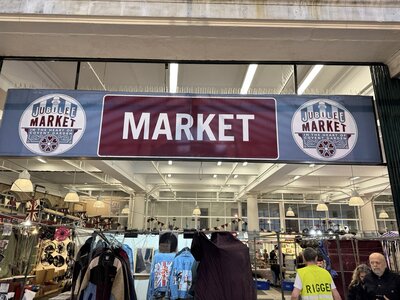 Burgundy red sign with white lettering JUBILEE MARKET mounted above market entrance, vintage circular logos, Covent Garden market hall signage