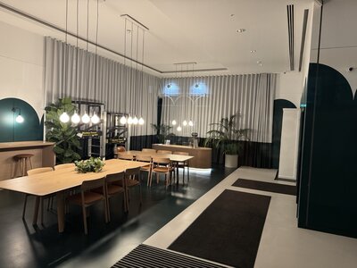 Modern conference dining room with long wooden tables, contemporary designer pendant lighting hanging from ceiling, floor-to-ceiling curtains, minimalist interior for meetings