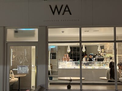 WA Japanese Patisserie storefront window at night, warm interior lighting, minimalist white pendant lamps, staff behind contemporary counter, clean aesthetic