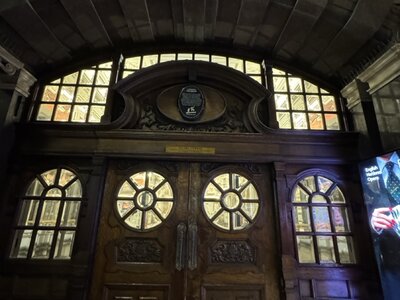 Historic monumental wooden entrance door with intricate circular window panels, ornamental glazing, arched fanlight above, commemorative plaque, grand institutional architecture