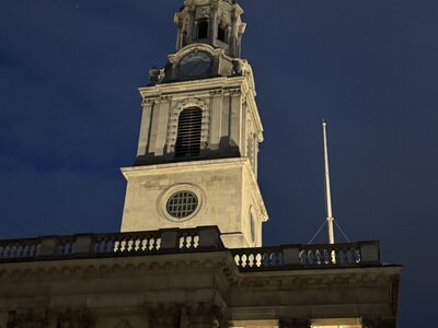 Nighttime St Martin-in-the-Fields with illuminated white stone tower, functioning clock, pointed spire, neoclassical elements against dark blue sky