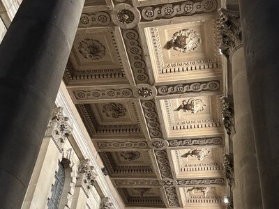 Ornate neoclassical interior ceiling with elaborate coffered panels, decorative relief moldings, towering Corinthian columns, acanthus leaf capitals, gilded details