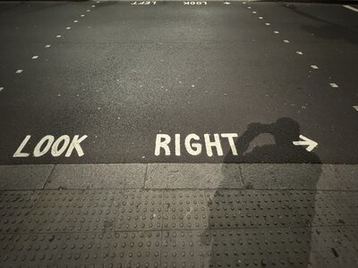 Large white LOOK RIGHT road surface marking with directional arrow painted on dark asphalt, grey tactile paving for visually impaired pedestrians along curb