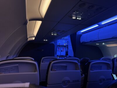 Empty aircraft cabin at night with atmospheric blue LED mood lighting, rows of passenger seats with headrest entertainment systems, tranquil ambiance during homeward flight